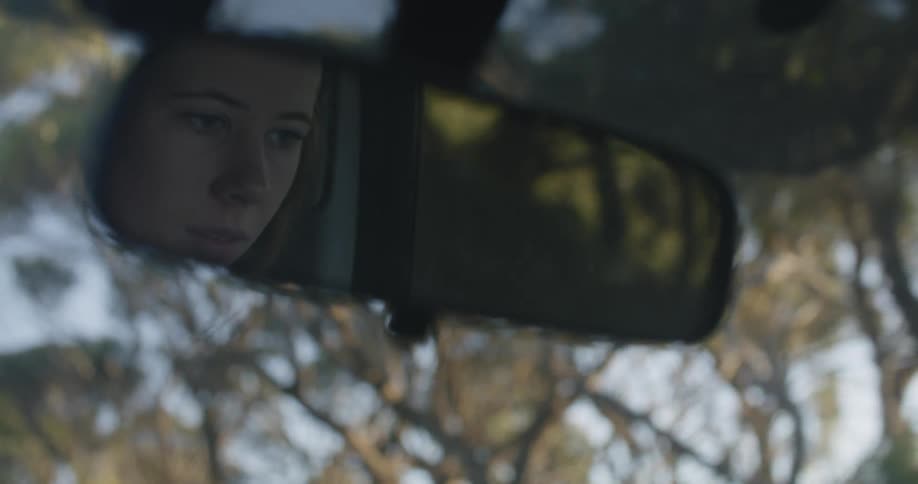 Reflection on a rear view mirror of a woman driving a car at morning