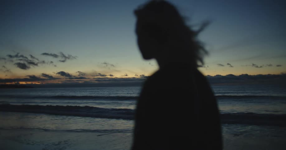 Silhouette of a woman walking on a beach and her hair blowing in the breeze as the waves roll in