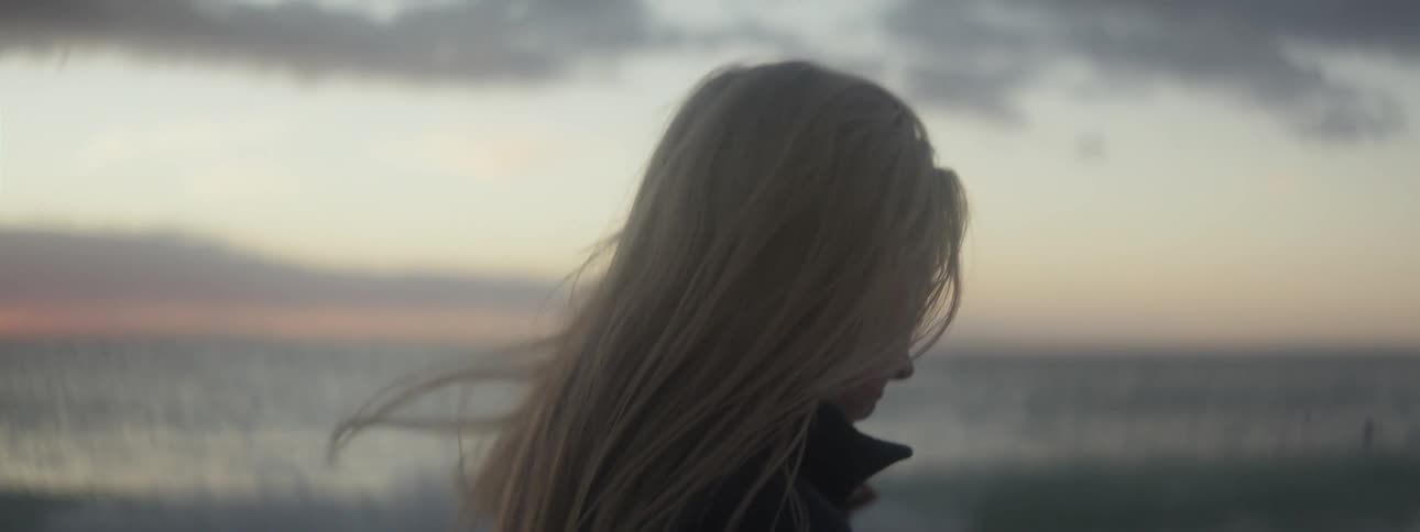 A woman is walking on a beach and her hair is blowing in the breeze as the waves roll into shore