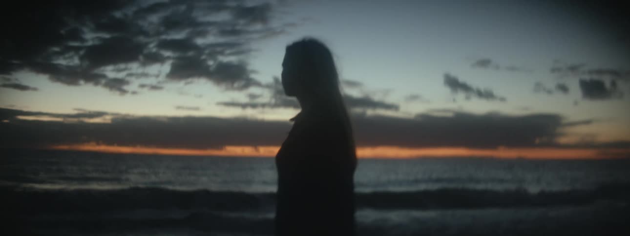 Silhouette of a woman walking on a beach and her hair is blowing in the breeze as the waves roll in