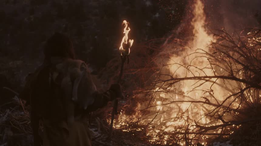 Man standing near pile of branches on fire at night