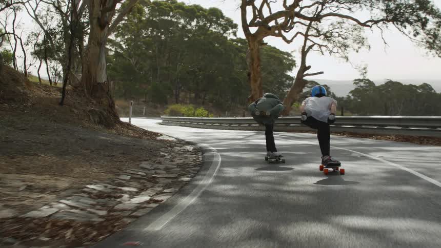 Couple of teenagers rolling on skateboards downhill on a road next to the ocean