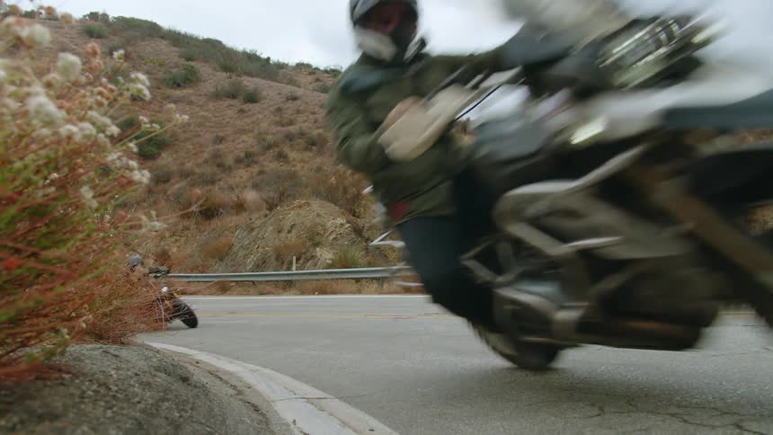 Two people riding motorcycles on a road downhill in the mountains
