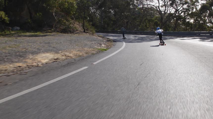 Two people skateboard down a street
