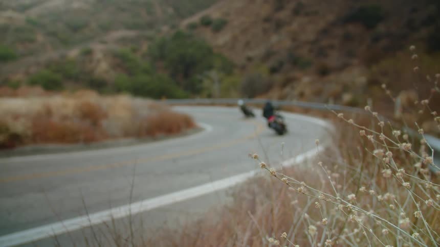 Two people drive motorcycles down a road