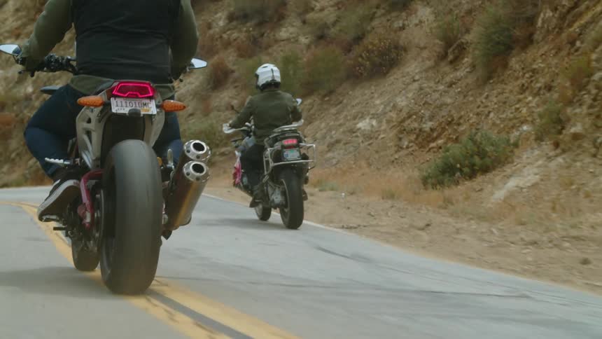 Two people driving motorcycles down a street