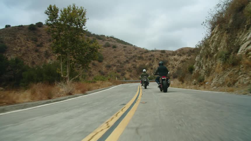 Two motorcyclists ride down a rural highway