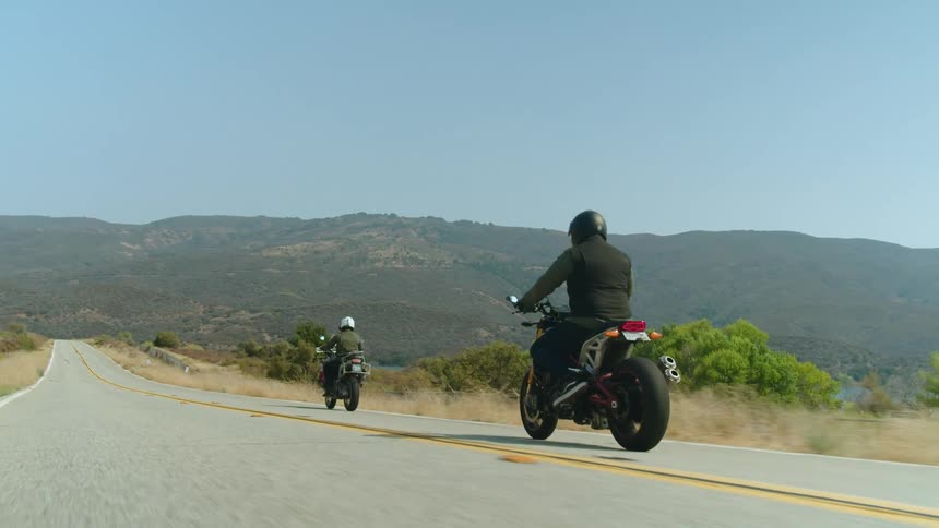 Two men drive motorcycles down a road