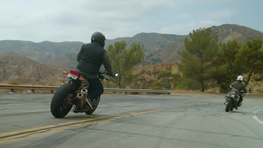 Two people drive motorcycles down a road