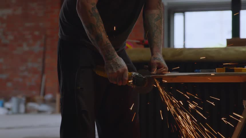 Sparks fly as a man uses a grinding tool on metal in a warehouse