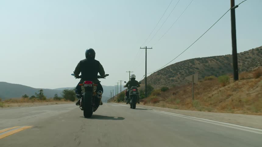 Two motorcyclists ride down a rural highway