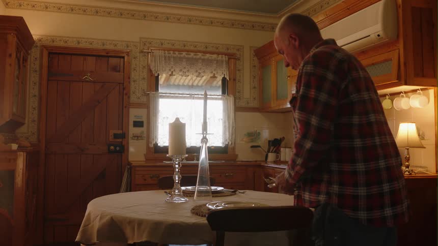 Older man sets table standing in kitchen