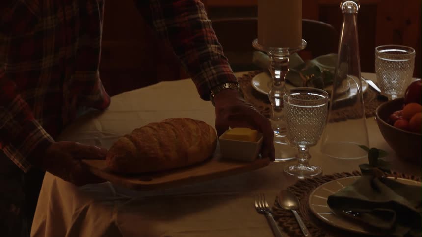 A man carries a loaf of fresh baked bread to the dining room table