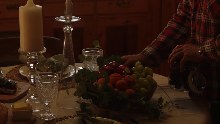 A man arranges a fruit tray on a table set for a candlelight dinner