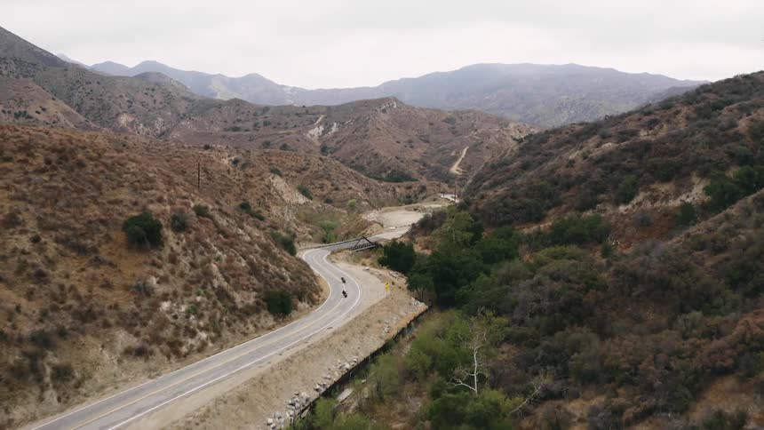 Two motorcyclists ride down a curvy road through mountains