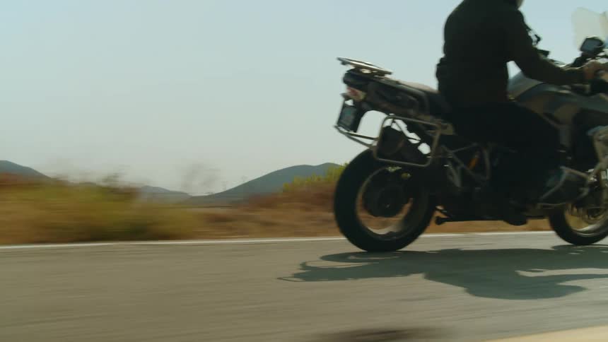 A motorcycle travels on a road with mountains in the distance