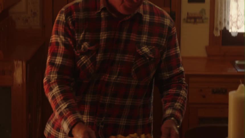 A man carries and places a casserole dish on the table next to home baked bread on a cutting board