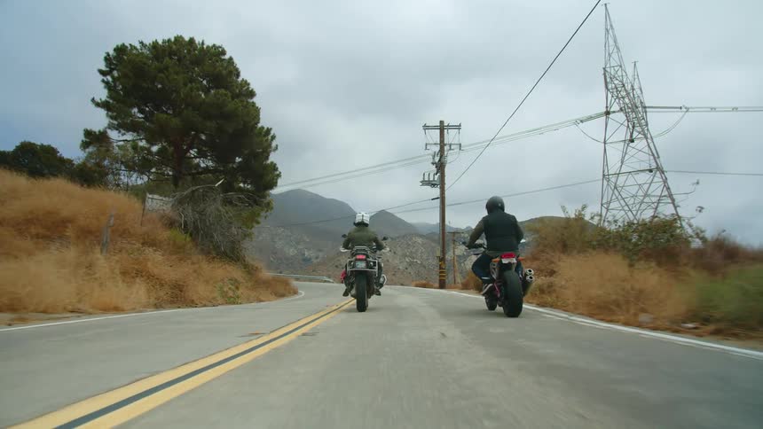 Bikers ride motorcycles on country road on cloudy day