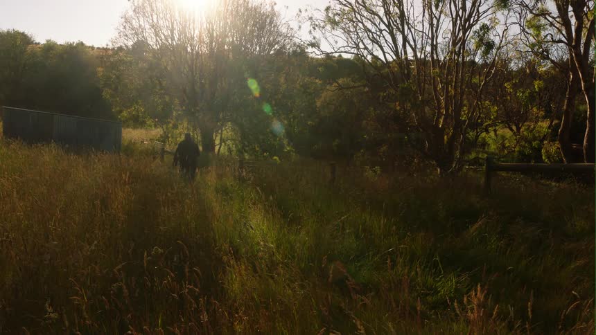 A man carries a fishing pole across a field