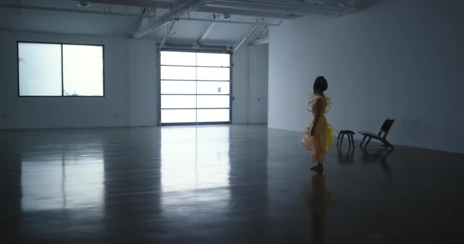 Female model with frizzy hair makeup with glitters and yellow dress stands still in empty room