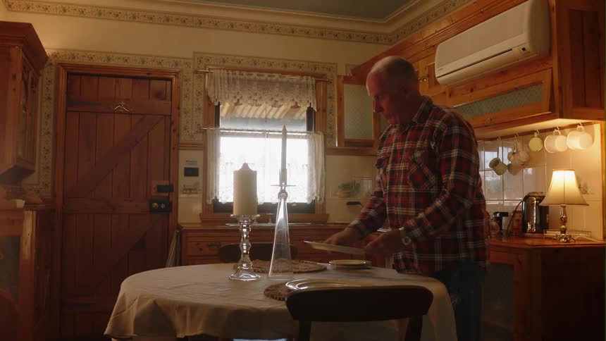 An elderly man sets a table at home