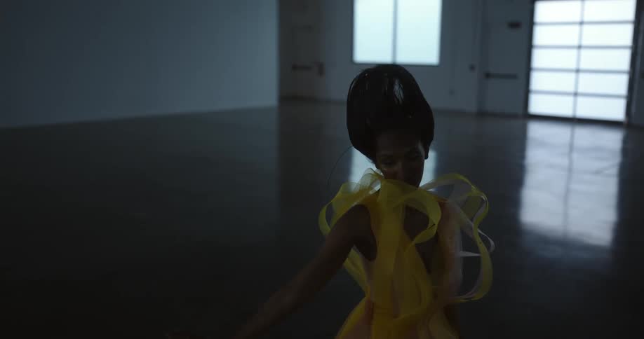 Female model with frizzy hair makeup with glitters and yellow dress dances in empty room