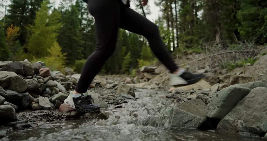 A woman hiking crosses over a river