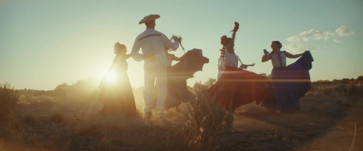 Folk dancers in traditional costume perform folk dance in field while backlit by the sun