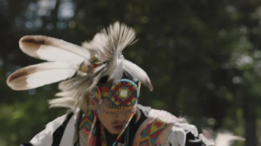A festively dressed native american man performs a dance