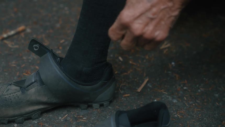 A man puts on cycling style shoes while outside