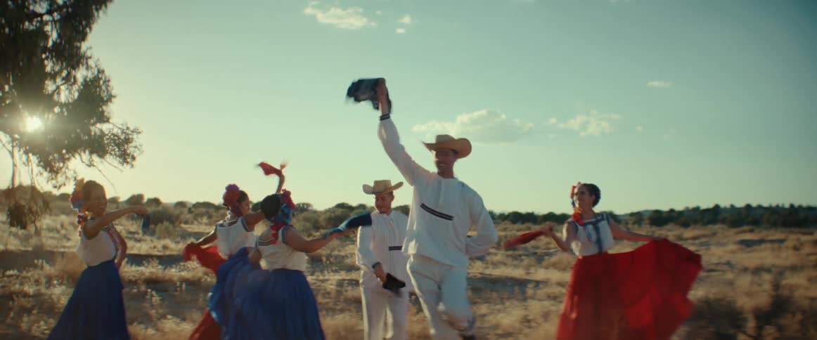 A group of men and women wearing traditional Mexican folk outfits dancing outdoors