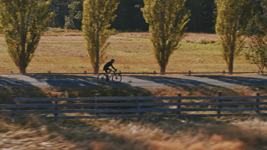 An older man focused on fitness rides his bike through the countryside next to a farm in sunset light