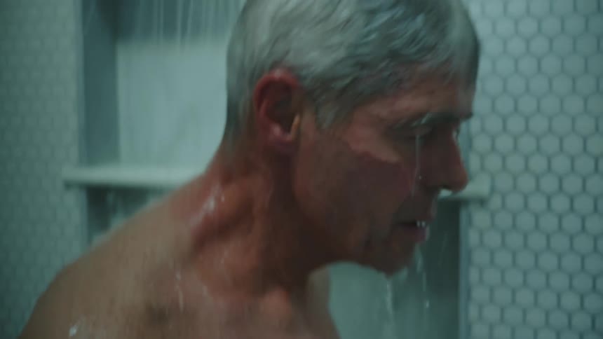 A man stands under running water in a shower at home