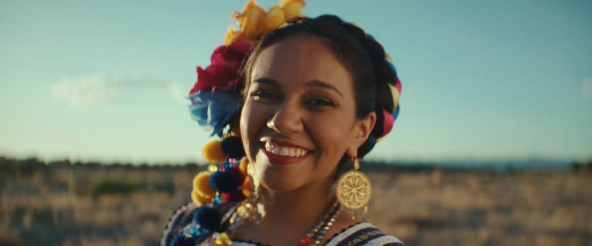 A woman smiles wide while posing in traditional Mexican clothing in a field