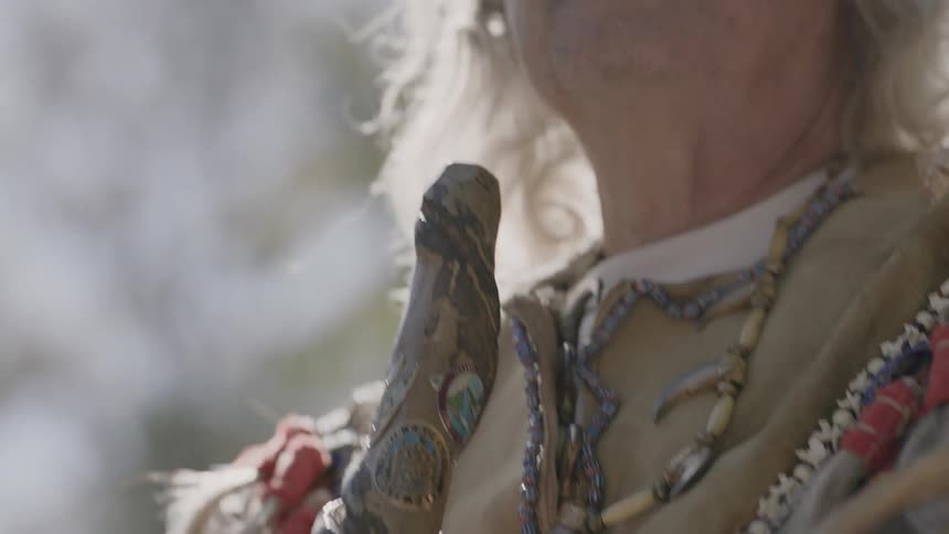 A native american man holds a decorated stick