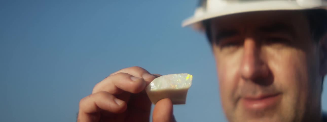 A man wearing a hardhat is looking at an opal stone in his hand