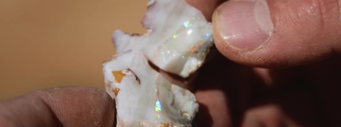A man separates a rock to show the opal inside