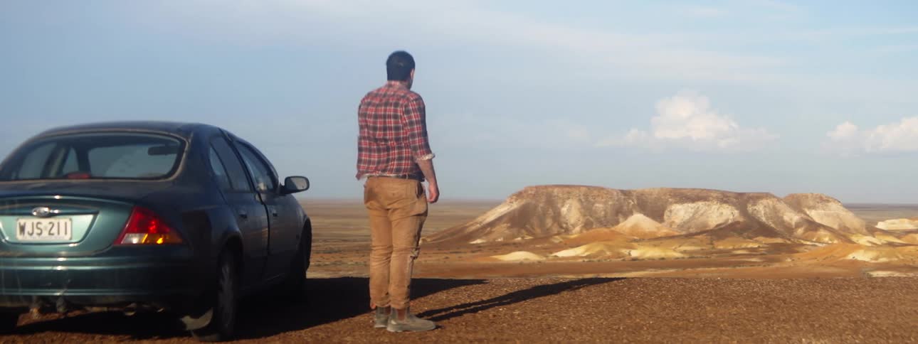 Man stands near parked car looking out at plateau topped lone mountain