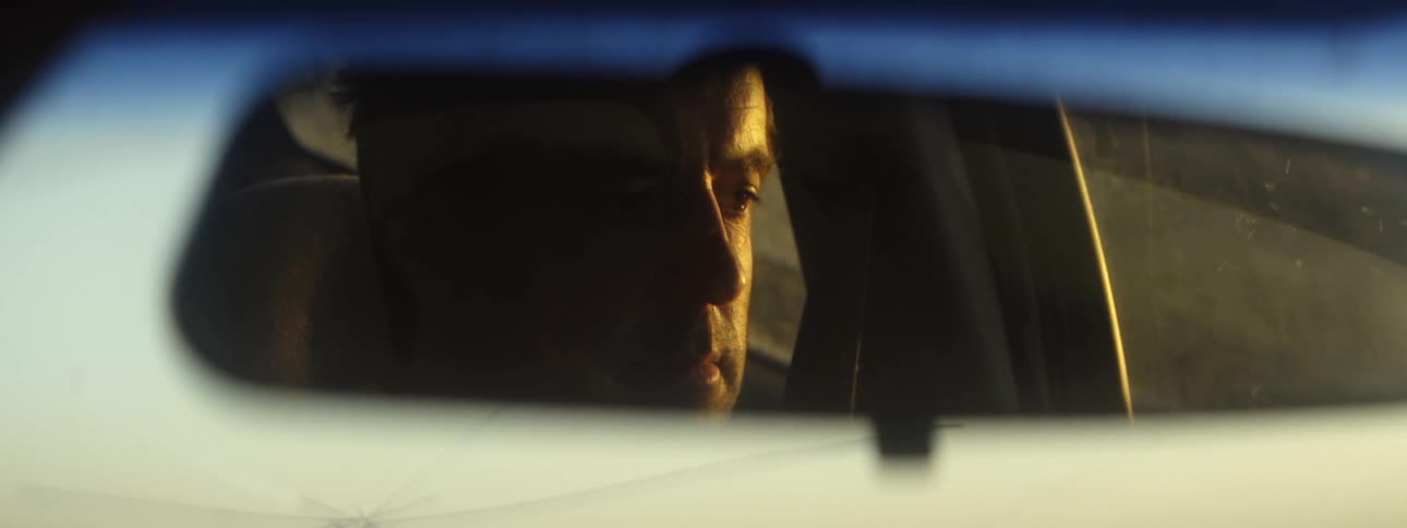 A man driving down a highway is visible in his rearview mirror