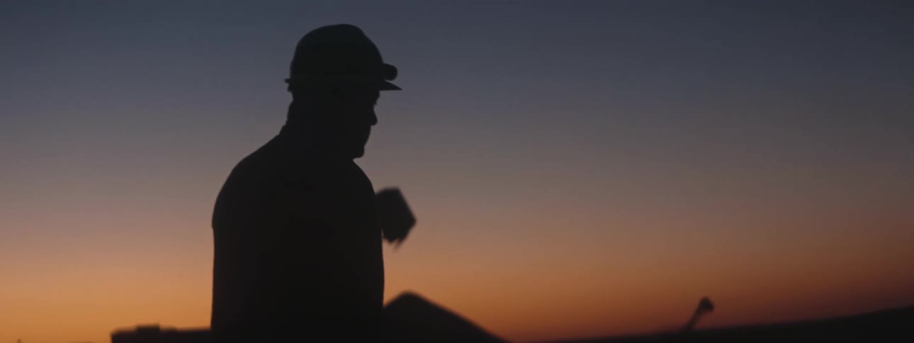 A man on a construction site stands in front of a construction crane