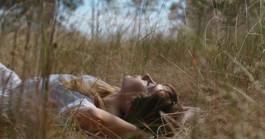 A woman lies in a grassy field with her eyes closed