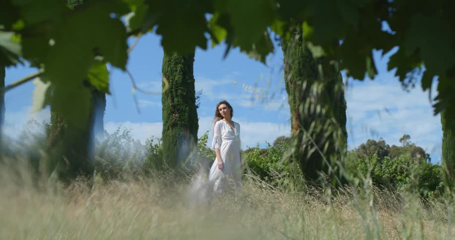 A woman stands under trees in a field as the wind blows