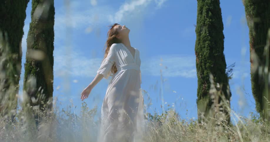 A woman throws her head and arms back while posing between tall trees