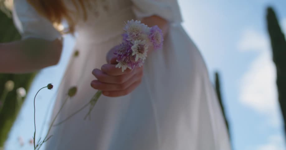A woman picks wildflowers while standing outside