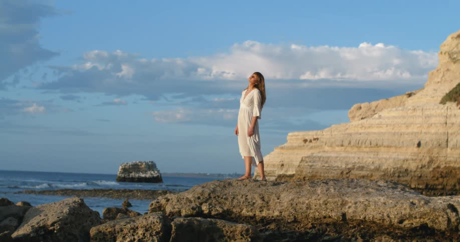 Woman stands on raised stone overlooking waves