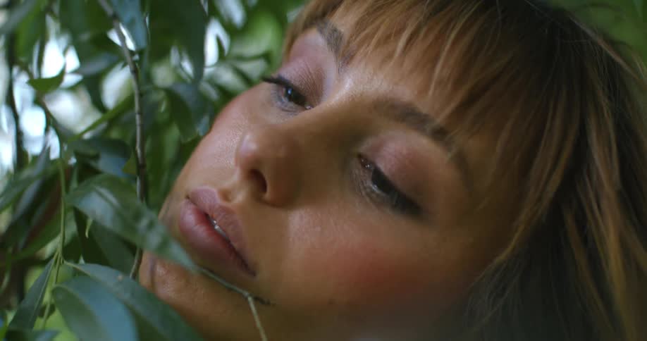 Woman brushes her face with tree branch