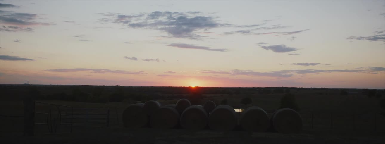 Sunsets on horizon over bales of hay