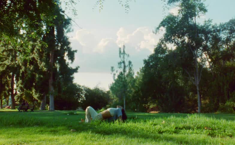 Woman dances in field in park as people sit on bench in background