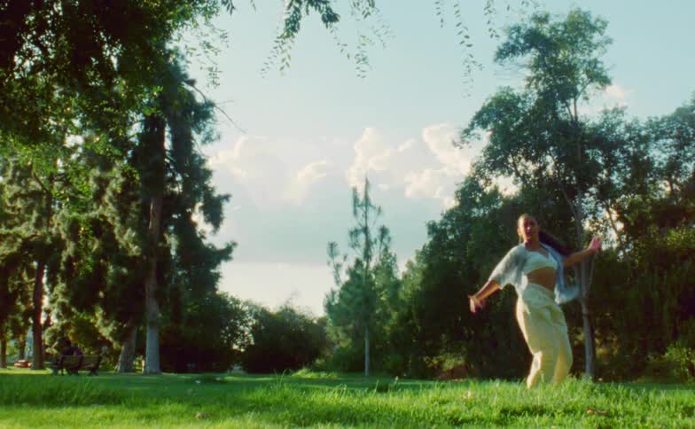 Female dancer with ponytail blue shirt white top and yellow pants dances in park
