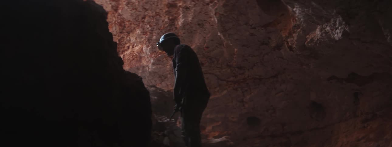 A miner is swinging a pickax at the rocks